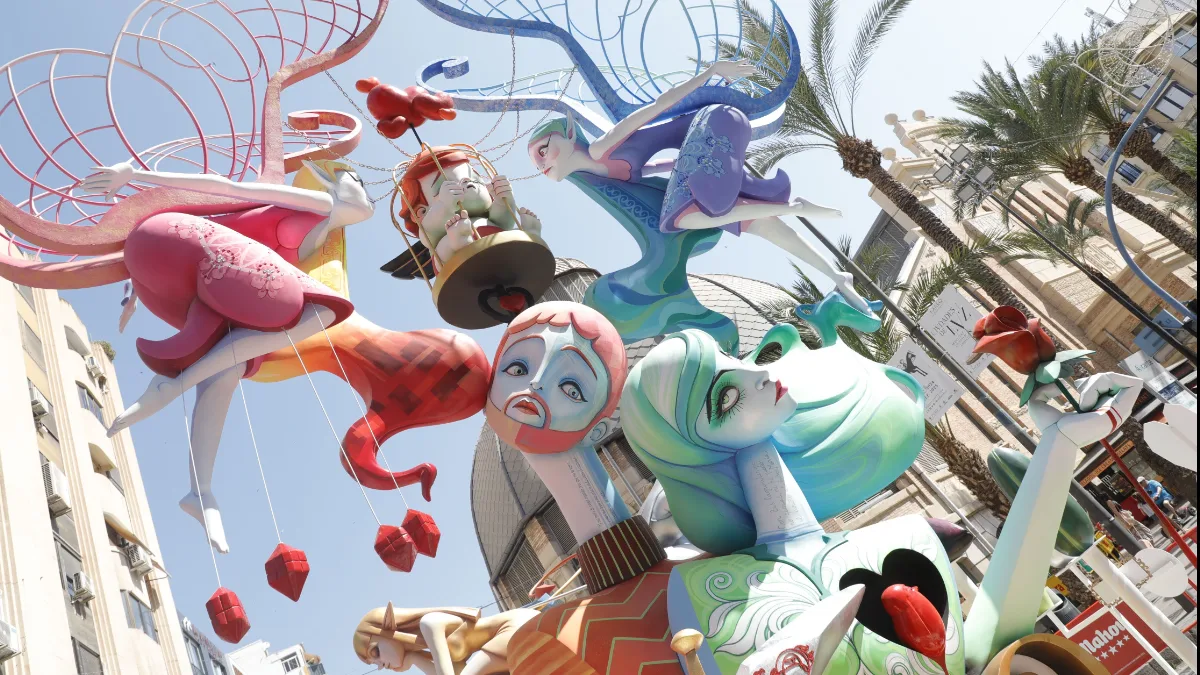 Las Fogueres de Sant Joan 2026 de Alicante son mucho más que cinco días de fiesta. El calendario festero arranca el 23 de mayo con la inauguración de la Exposición del Ninot y no termina hasta el 29 de junio con el Coso Multicolor — más de un mes de actos, desfiles, mascletàs y pólvora que transforman la ciudad semana a semana. El arranque oficial llega este viernes 5 de junio con el Pregón de Fiestas desde la Plaza del Ayuntamiento. Declaradas Fiesta de Interés Turístico Internacional, las Fogueres afectan a la movilidad de Alicante durante semanas — aquí tienes el programa completo y todo lo que necesitas saber para moverte. Programa oficial de las Fogueres de Sant Joan 2026 Miércoles 3 de junio — Encendido del alumbrado festero A las 21:30 horas, encendido oficial del alumbrado festero en la plaza del Ayuntamiento (por confirmar). Más de 650.000 luces LED iluminarán la ciudad durante las celebraciones. Viernes 5 de junio — Pregón: inicio oficial de las fiestas A las 18:30 horas, evento 'Música per a una Festa' con 1.100 músicos y 25 bandas congregados en la Plaza de España. A las 19:00 horas, Homenaje al Foguerer y Barraquer fallecidos en la Plaza de España. A las 19:30 horas, Desfile del Pregón entre la Plaza de España y la Plaza del Ayuntamiento. A las 21:00 horas, Pregón de Fiestas desde la Plaza del Ayuntamiento. A las 23:00 horas, Fiesta del Pregón en la Zona Volvo. El pregonero de 2026 es el artista alicantino de pop urbano Funzo. Sábado 6 de junio — Desfile del Ninot A las 19:00 horas, Desfile del Ninot a través del itinerario oficial entre Luceros y el Ayuntamiento. Las comisiones desfilan disfrazadas con motivos alegóricos al tema de su hoguera — uno de los desfiles más originales y divertidos de toda la fiesta. Domingo 7 de junio — Mascletà y Mostra de Folklore A las 14:00 horas, mascletà del ciclo 'Pólvora tot l'any' en avenida Unicef 6. A las 18:00 horas, III Mostra de Folklore Alacantí en la avenida de la Constitución: cuentacuentos, talleres de dansà, juegos tradicionales, artesanía y actuaciones de grupos de danzas locales y la Colla de Nanos i Gegants d'Alacant. Sábado 13 de junio — Entrada de Bandas A las 14:00 horas, mascletà en el centro comercial Gran Vía (plaza Agatangelo Soler). A las 19:00 horas, Entrada de Bandas y comisiones a través del itinerario oficial. Uno de los desfiles más esperados de toda la fiesta — decenas de bandas de música desfilan por el centro de Alicante con las comisiones de cada hoguera. Domingo 14 de junio — Clausura de la Exposición del Ninot A las 20:00 horas, clausura de la Exposición del Ninot y entrega de premios para conocer el Ninot Indultat 2026 tras el recuento de votos en la antigua Lonja del Pescado. El ninot indultat es el único monumento que se salva de la quema — elegido por votación popular. Miércoles 17 de junio — Arribada del Foc Por la tarde, colocación del remate de la Hoguera Oficial en la plaza del Ayuntamiento. A las 23:30 horas, espectáculo nocturno de luz y sonido 'Arribada del Foc' en la fachada de El Corte Inglés, frente a la plaza de la Estrella. Jueves 18 y viernes 19 de junio — Inicio del Concurso de Mascletàs en Luceros El jueves 18 a las 14:00 horas, primera mascletà en la Plaza de los Luceros (fuera de concurso), a cargo de Fuegos Artificiales del Mediterráneo. El viernes 19 a las 14:00 horas, segundo disparo del concurso oficial de mascletàs a cargo de Pirotecnia Crespo. A las 00:01 horas de la madrugada del viernes al sábado, plantà oficial de los monumentos infantiles y ninots al carrer. Sábado 20 de junio — Plantà de las hogueras adultas A las 00:01 horas de la madrugada del sábado al domingo, plantà oficial de las hogueras adultas y barracas. A las 9:00 horas, visita del jurado a las hogueras infantiles. A las 14:00 horas, tercera mascletà a cargo de Pirotecnia Turis. A las 17:00 horas, fallo del jurado de las hogueras infantiles. A las 20:30 horas, inauguración de Barracas y Racós. Domingo 21 de junio — Primera Ofrenda de Flores A las 00:01 horas, plantà oficial de las hogueras adultas. A las 9:00 horas, visita del jurado a las hogueras adultas. A las 14:00 horas, cuarta mascletà a cargo de Fuegos Artificiales del Mediterráneo. A las 17:00 horas, fallo del jurado adulto. A las 18:00 horas, primera sesión de la Ofrenda de Flores a la Virgen del Remedio a través de Alfonso El Sabio, la Rambla, calle San José, Concatedral, San Nicolás, Rafael Altamira y Plaza del Ayuntamiento. Lunes 22 de junio — Desfile de premios y segunda Ofrenda A las 11:00 horas, desfile de entrega de premios desde el Ayuntamiento hasta la Rambla. A las 13:00 horas, Colla de Nanos i Gegants. A las 14:00 horas, quinta mascletà a cargo de Pirotecnia Pibierzo. A las 18:00 horas, segunda sesión de la Ofrenda de Flores. Martes 23 de junio — Desfile Folclórico Internacional A las 12:30 horas, entrega de premios de la Ofrenda de Flores en el Mercadito de Fogueres. A las 14:00 horas, sexta mascletà a cargo de los Hermanos Ferrández. A las 18:00 horas, Dansà d'Alacant en torno a la Hoguera Oficial en la plaza del Ayuntamiento. A las 19:00 horas, Desfile Folclórico Internacional por el recorrido oficial entre Luceros y Ayuntamiento. Miércoles 24 de junio — San Juan: la Nit de la Cremà A las 14:00 horas, séptima y última mascletà a cargo de Pirotecnia Alta Palancia. A las 20:00 horas, misa oficial de Fogueres en la Concatedral de San Nicolás. A las 00:00 horas, disparo de la monumental Palmera desde la cumbre del Monte Benacantil a cargo de Pirotecnia Hermanos Ferrández, seguido del inicio de la Nit de la Cremà. La Hoguera Oficial en la plaza del Ayuntamiento es la primera en arder. Del 25 al 29 de junio — Fuegos artificiales y Coso Multicolor Entre el 25 y el 29 de junio, castillos de fuegos artificiales a las 00:00 horas desde el Postiguet, a la altura del Paseito Ramiro, en el nuevo emplazamiento autorizado por Costas tras la salida obligada de la playa del Cocó. El lunes 29 de junio, último gran acto con el Coso Multicolor — las Belleas y Damas de cada comisión llenarán de color y confeti las inmediaciones del Centro Comercial Gran Vía. Cortes de tráfico y movilidad durante las Fogueres Las Fogueres transforman completamente la movilidad de Alicante. Con 182 hogueras entre adultas e infantiles y cerca de medio centenar de portadas de barracas repartidas por toda la ciudad, cientos de calles quedan cortadas al tráfico rodado durante la semana grande. El Ayuntamiento establece un circuito permeable en el centro con la velocidad limitada a 20 km/h. La circulación perimetral se recomienda por la Vía Parque y las grandes avenidas periféricas. Los días de mayor impacto en el tráfico son el viernes 5 de junio — Desfile del Pregón cortando el eje Plaza de España-Rambla-Altamira desde las 19:30 —, el sábado 13 — Entrada de Bandas desde las 19:00 — y la madrugada del 23 al 24 de junio, cuando la cremà corta decenas de calles simultáneamente. El tráfico de paso desde Alicante con destino Valencia se desviará por itinerarios alternativos durante los días de mayores restricciones. Transporte público: TRAM y autobús reforzados El TRAM d'Alacant y los autobuses urbanos refuerzan sus frecuencias durante toda la semana grande con servicios especiales nocturnos — especialmente en las noches del 23 y 24 de junio. Las paradas del TRAM en el centro — Luceros y Mercado — son los mejores puntos de entrada al epicentro festivo. El Ayuntamiento recomienda dejar el coche en zonas periféricas y acceder al centro en transporte público. Fuente: Federació de Les Fogueres de Sant Joan d'Alacant, Ayuntamiento de Alicante, Alicante ExtraÚltima actualización: 26 de mayo de 2026